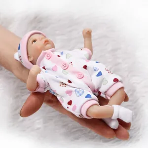 Miniature lifelike reborn baby doll in heart pattern romper held in palm of hand