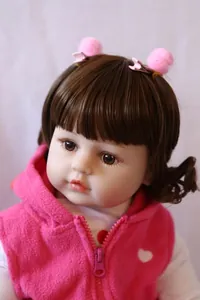 Detailed close-up of 60cm realistic baby doll with brown curls and pink fleece vest