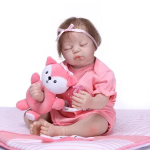 Realistic reborn baby doll sleeping in pink outfit with plush fox toy on striped cushion