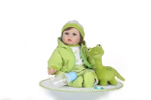 Detailed realistic reborn baby doll with green dinosaur outfit, plush toy and milk bottle