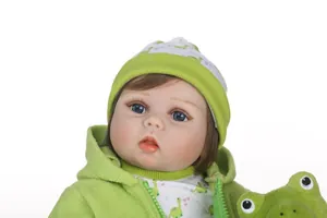 Close-up of lifelike baby doll with blue eyes, brown hair and green dinosaur outfit