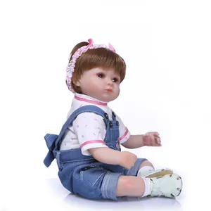 Poupée bébé réaliste avec cheveux bruns, chemise à fleurs et salopette en jean sur fond blanc