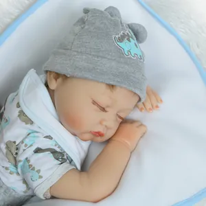 Dettaglio di una bambola reborn che dorme con cappello a dinosauro grigio e tutina blu