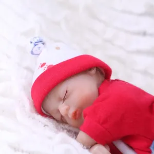 Lifelike sleeping reborn baby doll with red knit hat on soft white plush background