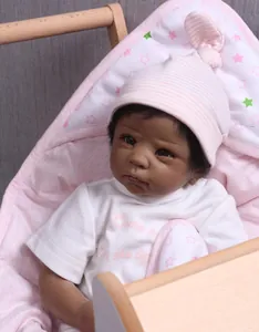 Realistic African reborn baby doll with brown eyes in a pink star pattern cradle