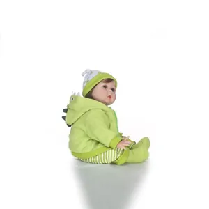 Realistic reborn baby doll in green dinosaur hoodie and striped pants on white background