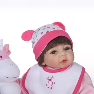 Realistic reborn baby doll in pink floral hat with plush unicorn on white background