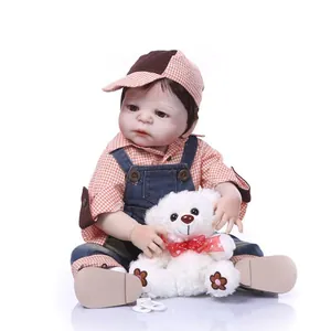 Poupée bébé réaliste avec chemise à carreaux et salopette en jean tenant un ours blanc