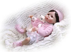 Realistic reborn baby doll in pink knit outfit holding a plush lamb on a soft white blanket