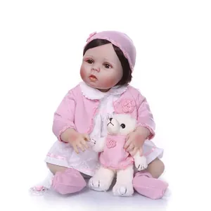 Realistic reborn baby doll in pink knit outfit with white teddy bear on white background