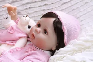 Detailed close-up of reborn baby doll with pink knitwear and a small plush teddy bear