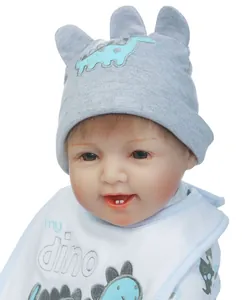 Dettaglio di una bambola reborn con cappello grigio da dinosauro e bavaglino bianco