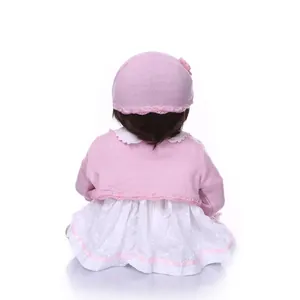 Detail view of a lifelike reborn baby doll back in pink knitted hat and lace dress