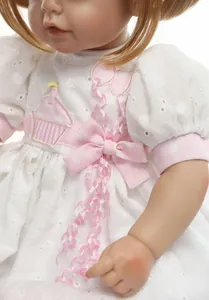 Detail showing high-quality embroidered white lace dress with pink ribbon on reborn baby doll