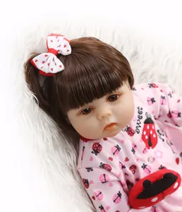 Close-up of realistic newborn baby doll with brown hair and pink ladybug sweet outfit