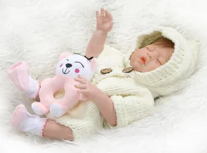 Detailed view of reborn baby doll in white knit romper holding a cat rattle toy