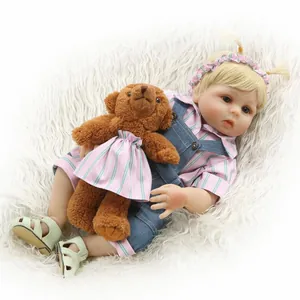 Poupée Reborn réaliste en salopette en jean avec ours en peluche sur tapis blanc