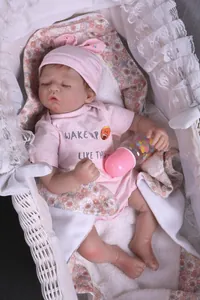 Close-up of sleeping reborn baby doll with pink rabbit hat and mini bottle in a basket