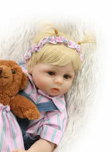Gros plan d'une poupée reborn réaliste avec couettes blondes et salopette tenant un ours