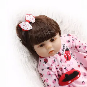 Realistic silicone baby doll in pink ladybug outfit with bow clip on plush background