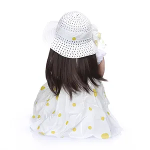 Realistic reborn doll with long brown hair in a yellow polka dot dress and straw hat