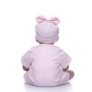 Rear view of a lifelike reborn baby doll in a pink short-sleeve bodysuit and floral bow hat