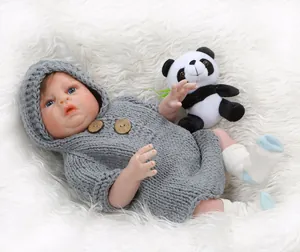 Detail of reborn baby doll in grey knit hoodie on plush background with panda toy