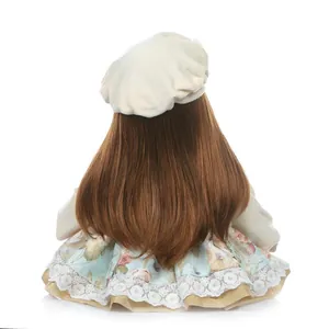 Reborn toddler doll with long dark brown hair in floral dress and beige beret back view