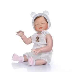 Realistic reborn baby doll in white knit romper and bear ear hat on white background