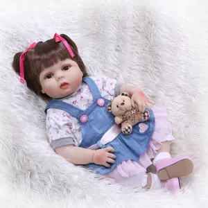 Realistic reborn baby doll with brown hair, floral dress and mini teddy bear on white rug