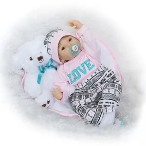 Lifelike soft vinyl baby doll in pink love outfit with plush bear on white background