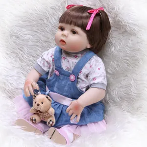 Lifelike reborn baby doll in floral outfit with denim dress and small teddy bear