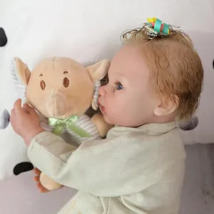 Lifelike reborn baby doll with blonde curls holding a plush elephant toy in green outfit