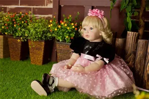 Detailed outdoor view of a lifelike reborn doll with golden curls sitting on green grass