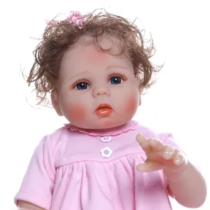 Realistic reborn baby doll with brown curly hair and pink dress on white background