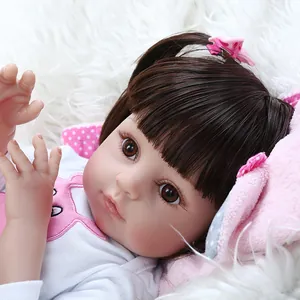 Lifelike reborn doll with brown hair and pink bow headband on white plush background