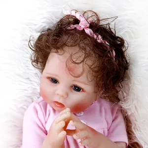 Close-up of lifelike reborn baby doll with brown curls, blue eyes and pink headband