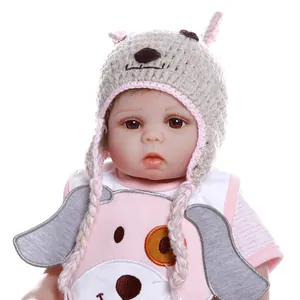 Lifelike reborn baby doll in pink cartoon outfit with knitted animal hat on white background