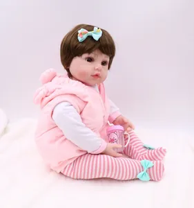 Detail of reborn baby doll with brown hair, pink plush vest and piggy baby bottle