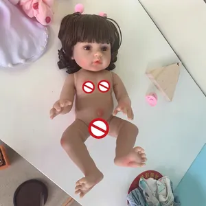 Realistic reborn baby doll with brown curly hair and pink hairpins on white surface