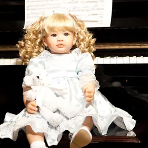 60cm realistic reborn baby doll with blonde curls and blue dress sitting by a piano