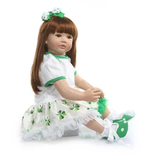 Realistic reborn toddler doll in clover print dress and green bow sitting on white background