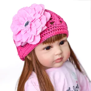 Handmade crochet baby hat with large pink flower on long-haired reborn doll head