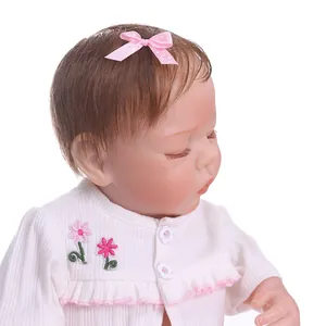 Detailed close-up of a sleeping reborn baby doll with floral embroidery and pink bow
