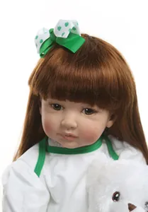Close-up of realistic reborn doll with brown hair, clover bow and white plush bear