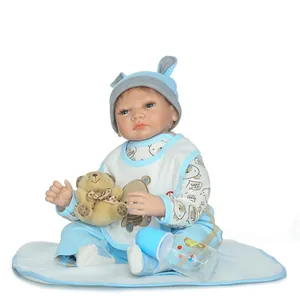 Muñeca Reborn con traje azul, osito de peluche y biberón sobre fondo blanco puro