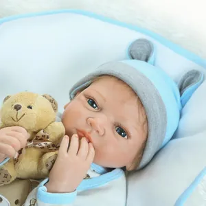 Muñeco bebé Reborn realista con traje de punto azul y osito sobre fondo de felpa suave