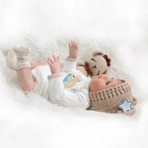 Bambola realistica reborn in pagliaccetto bianco a maglia con orsetto su tappeto