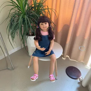 Lifelike 98cm toddler doll in pink shirt and denim dress seated on a white stool
