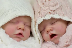Detail of twin reborn dolls with realistic skin texture and knitted caps on soft blankets